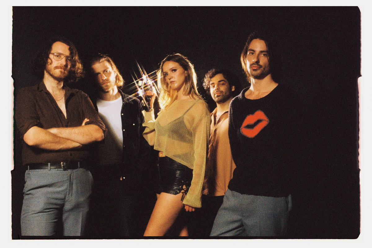 Romero promotional picture. The five band members all facing the camera, stood against a black backdrop. Singer Alanna Oliver is in the middle, flanked by a further two band members on either side of her. She is holding a tambourine that's glinting under the studio lights.